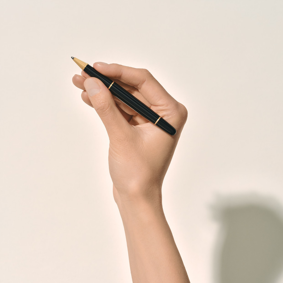 Hand holding the Montblanc Meisterstück Gold-Coated Classique rollerball pen with glossy black resin finish and gold-coated trim.