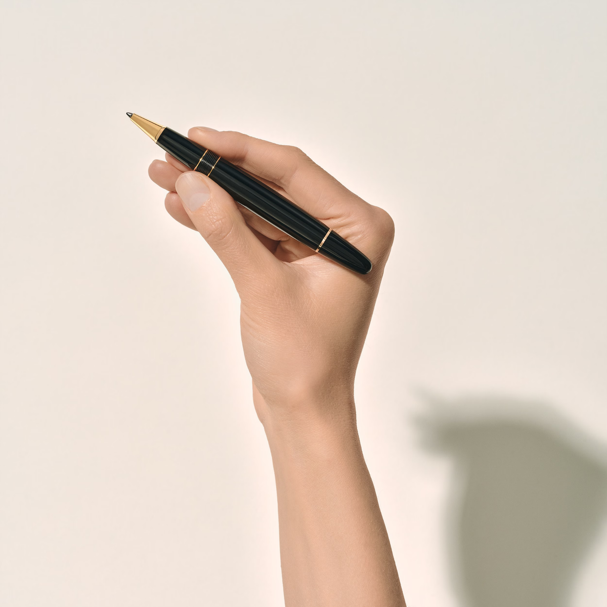 Hand holding the Montblanc Meisterstück Gold-Coated LeGrand rollerball pen with glossy black resin finish and gold-coated trim.