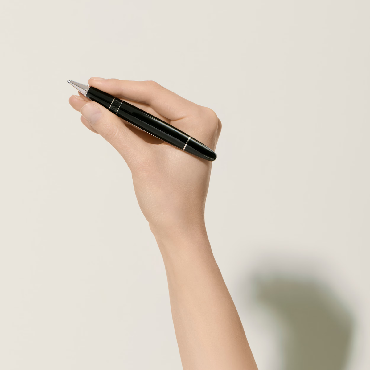 Hand holding the Montblanc Meisterstück Platinum-Coated LeGrand rollerball pen with glossy black resin finish and platinum-coated trim.