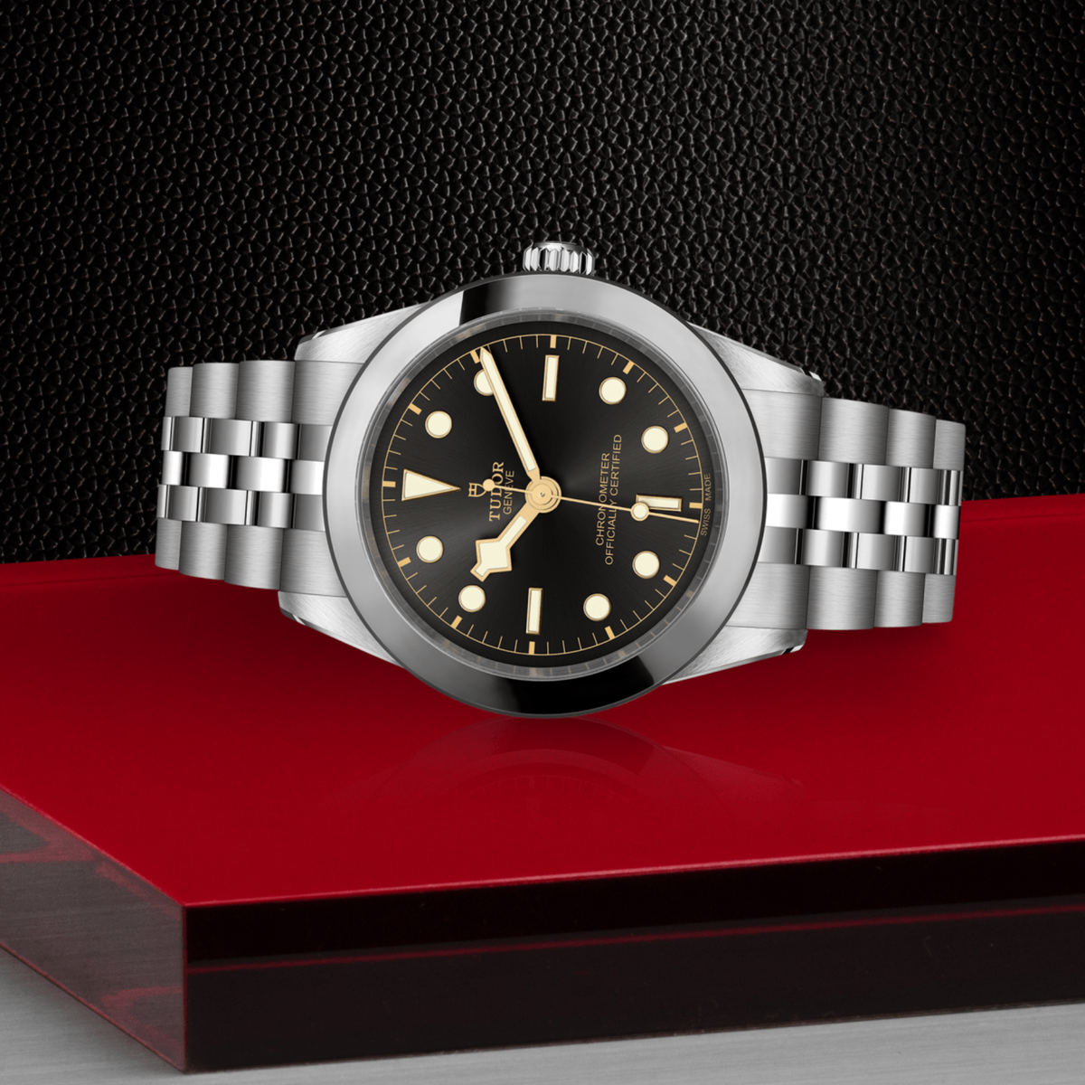 Silver watch with black dial on a red platform against a dark background