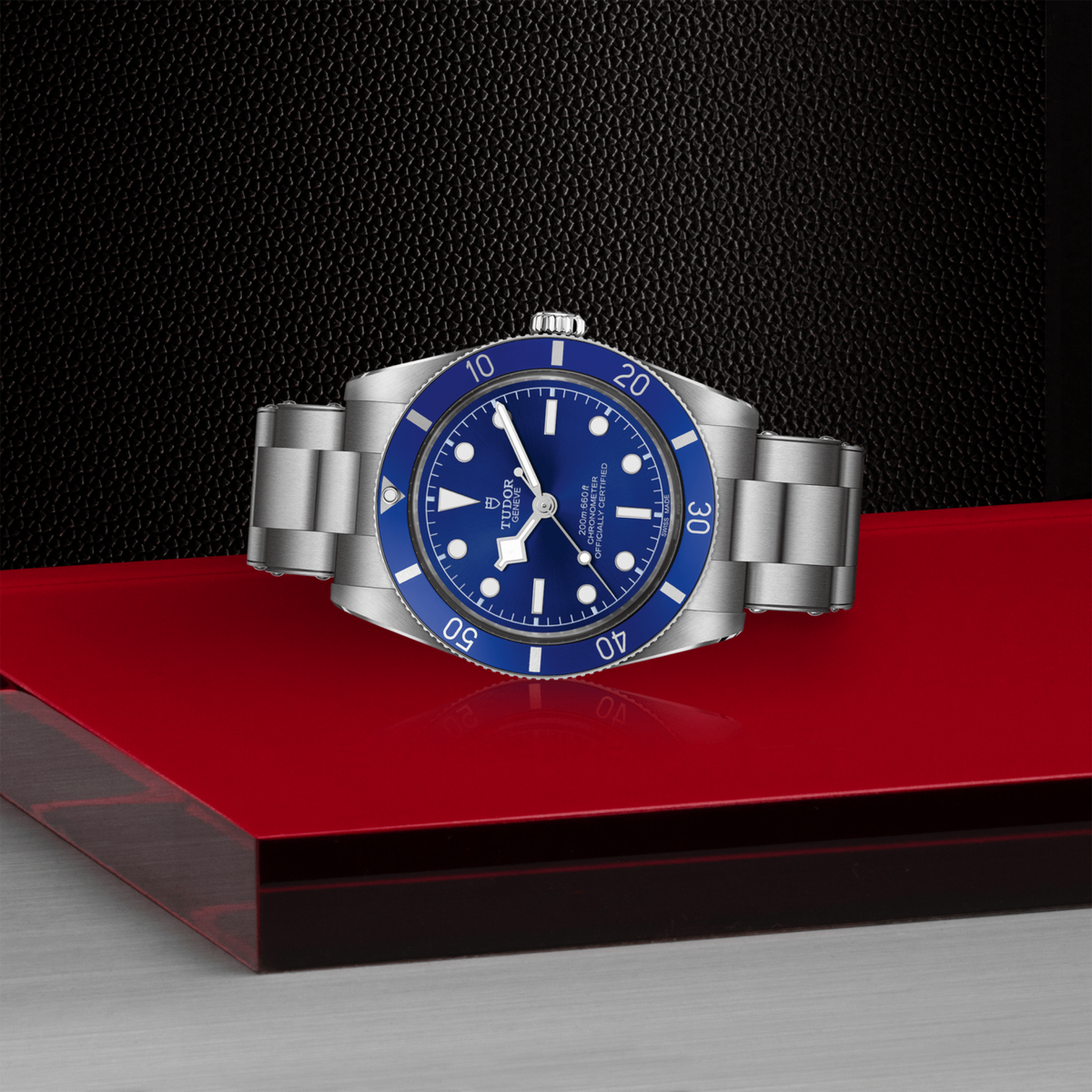 Silver watch with blue face on a red platform against a black background