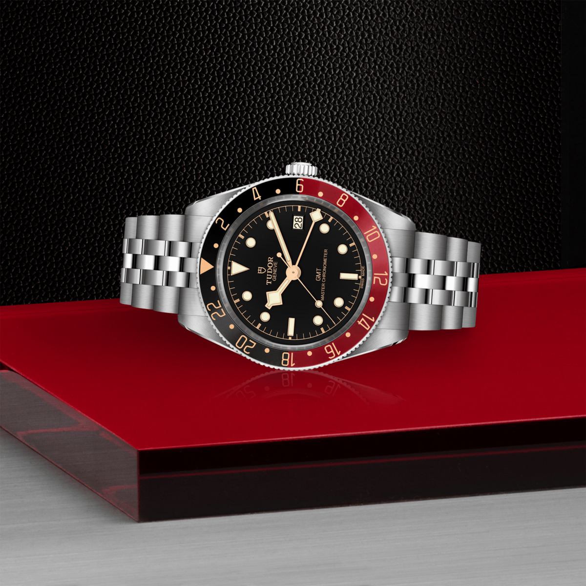 Watch with a silver band and black face on a red platform against a dark background