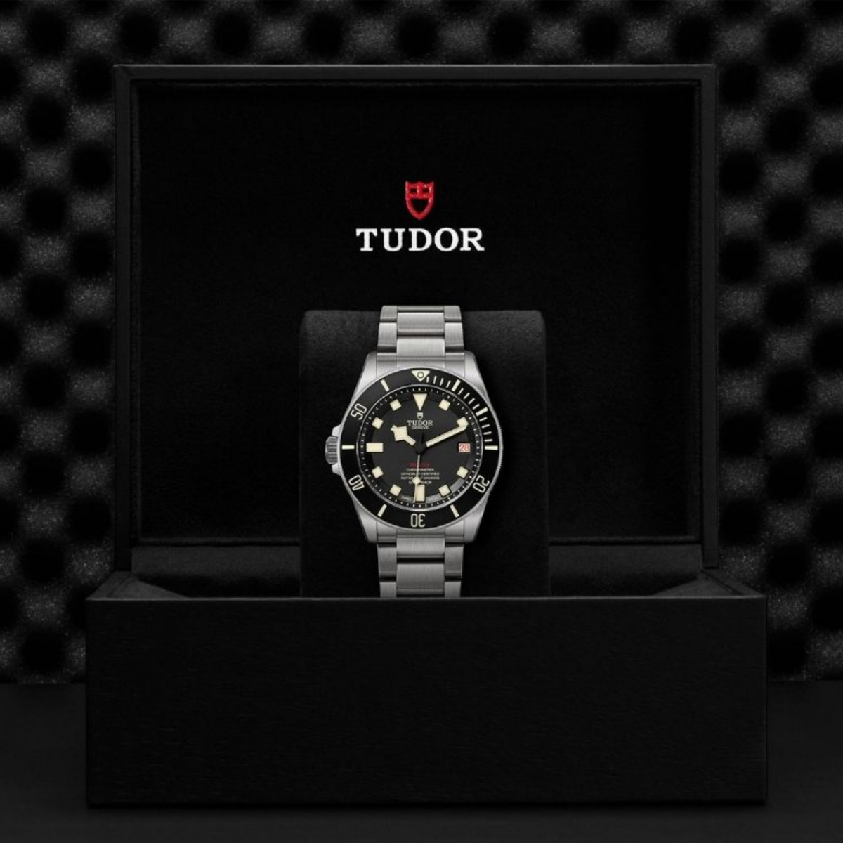 Tudor Pelagos dive watch with a titanium bracelet presented inside an open black Tudor display box with the Tudor logo in the background.
