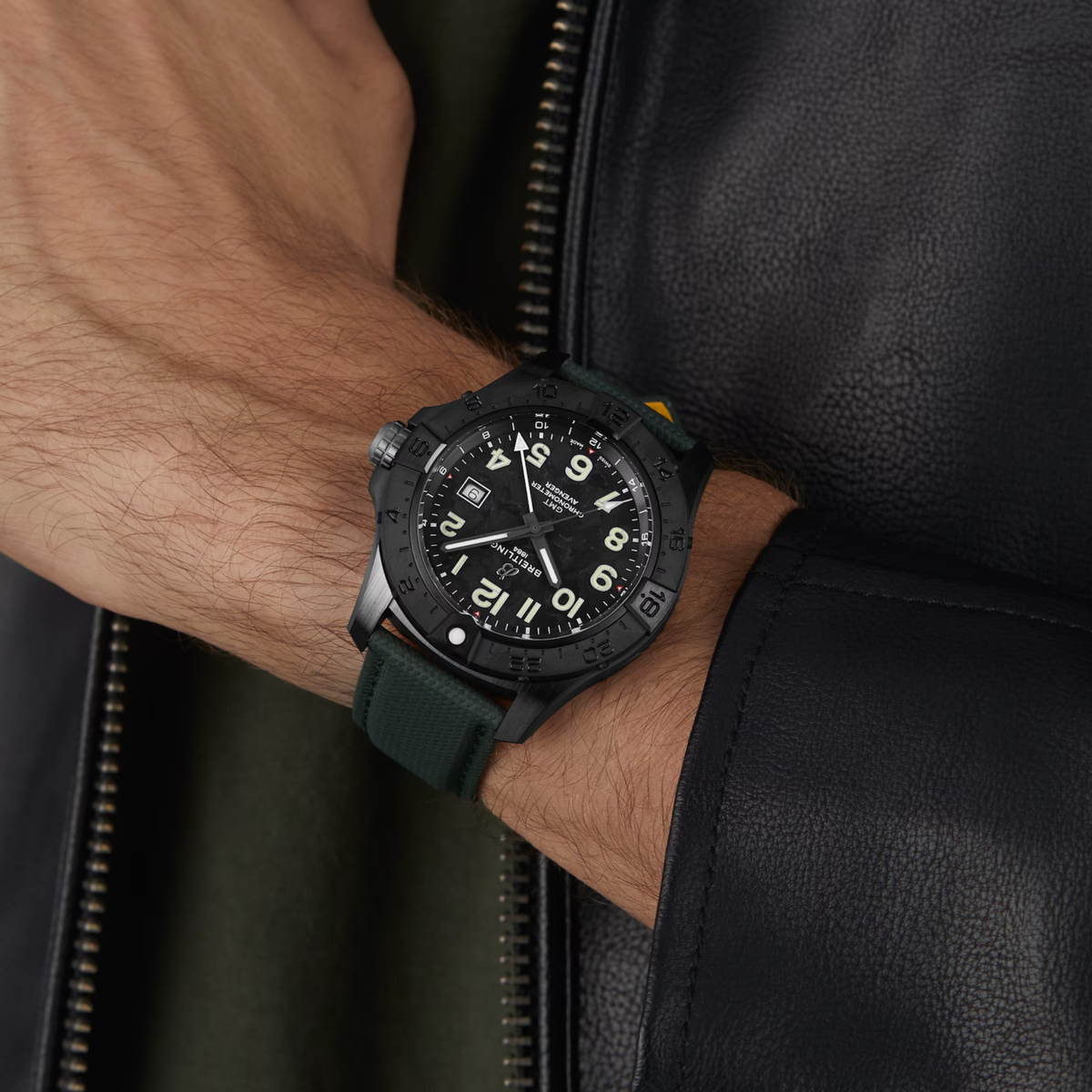 Black Breitling watch with green strap on wrist, worn with leather jacket