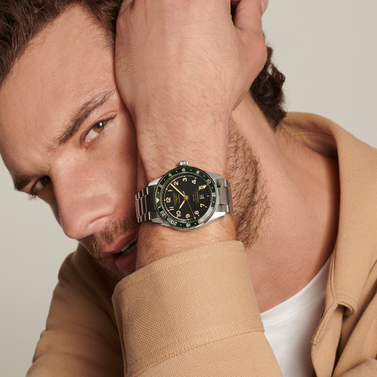 lifestyle image of Longines black dial GMT watch worn on a wrist showcasing the green ceramic bezel and sporty steel bracelet
