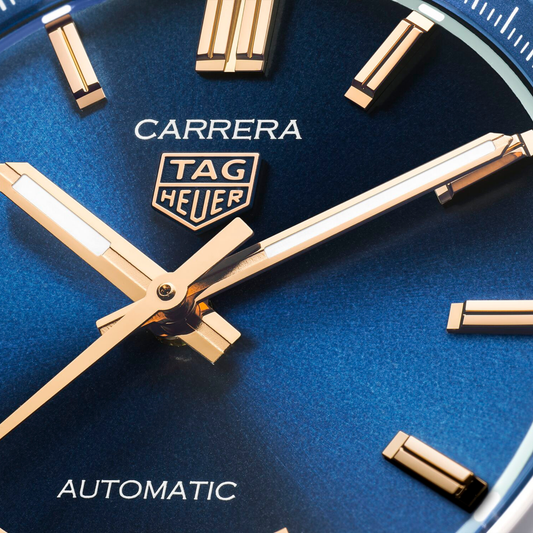 close-up of the blue dial showcasing the sunray finish, applied gold-tone indices, slim hands and date window at 6 o’clock