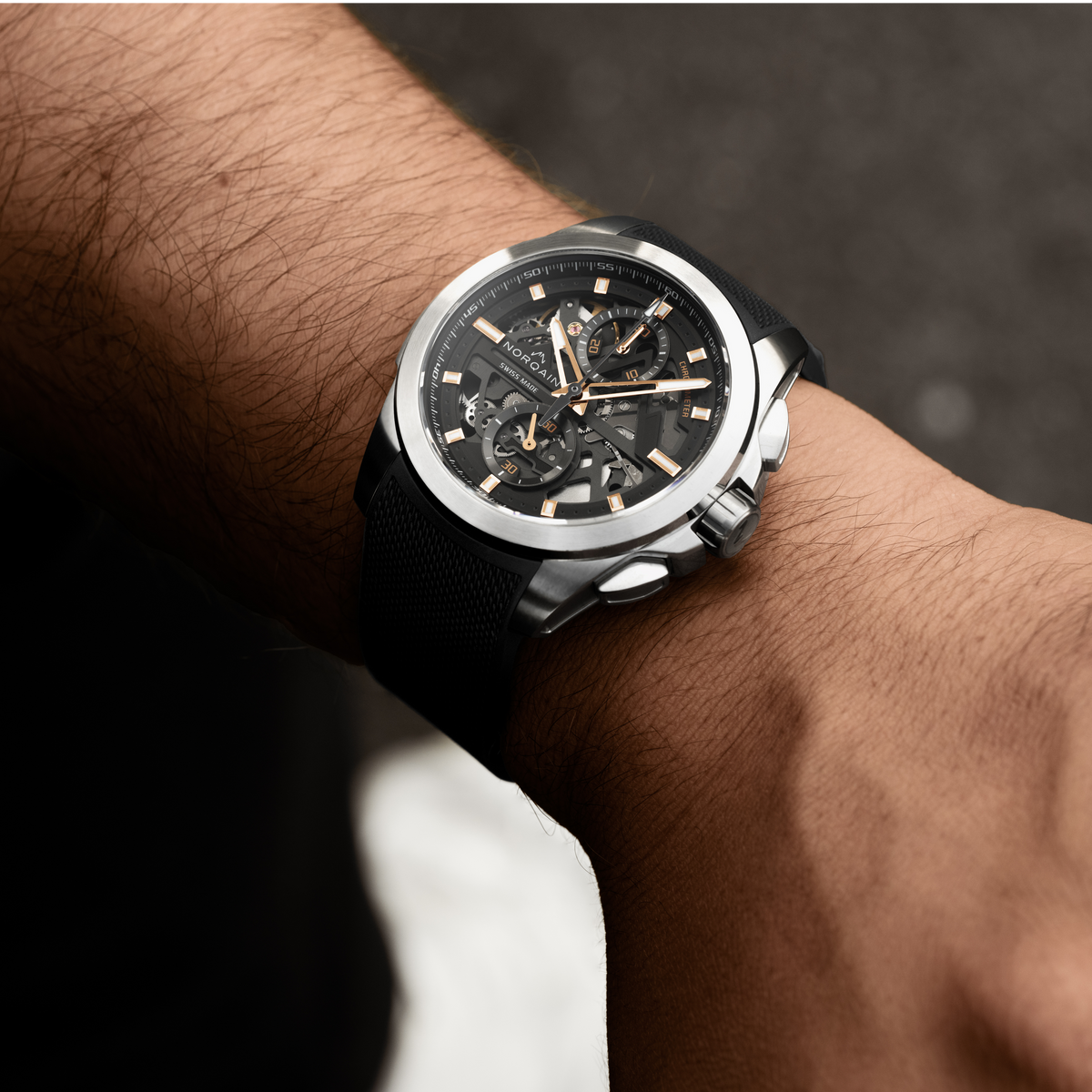 Close-up of the Norqain automatic skeleton chronograph showcasing exposed gears, twin chronograph sub-dials, luminous rose gold-tone hands and a brushed stainless steel case.
