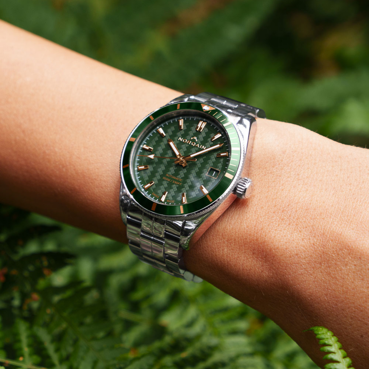 Angled view of the Norqain Independence Automatic Green Watch showcasing the patterned green dial, polished stainless steel case, rose gold-tone hands and integrated sporty bracelet design.