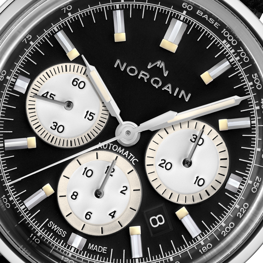Close-up detail of the Norqain Freedom 60 Chronograph with black dial, silver panda-style sub-dials, luminous hands and markers, date window and Swiss automatic chronograph movement.