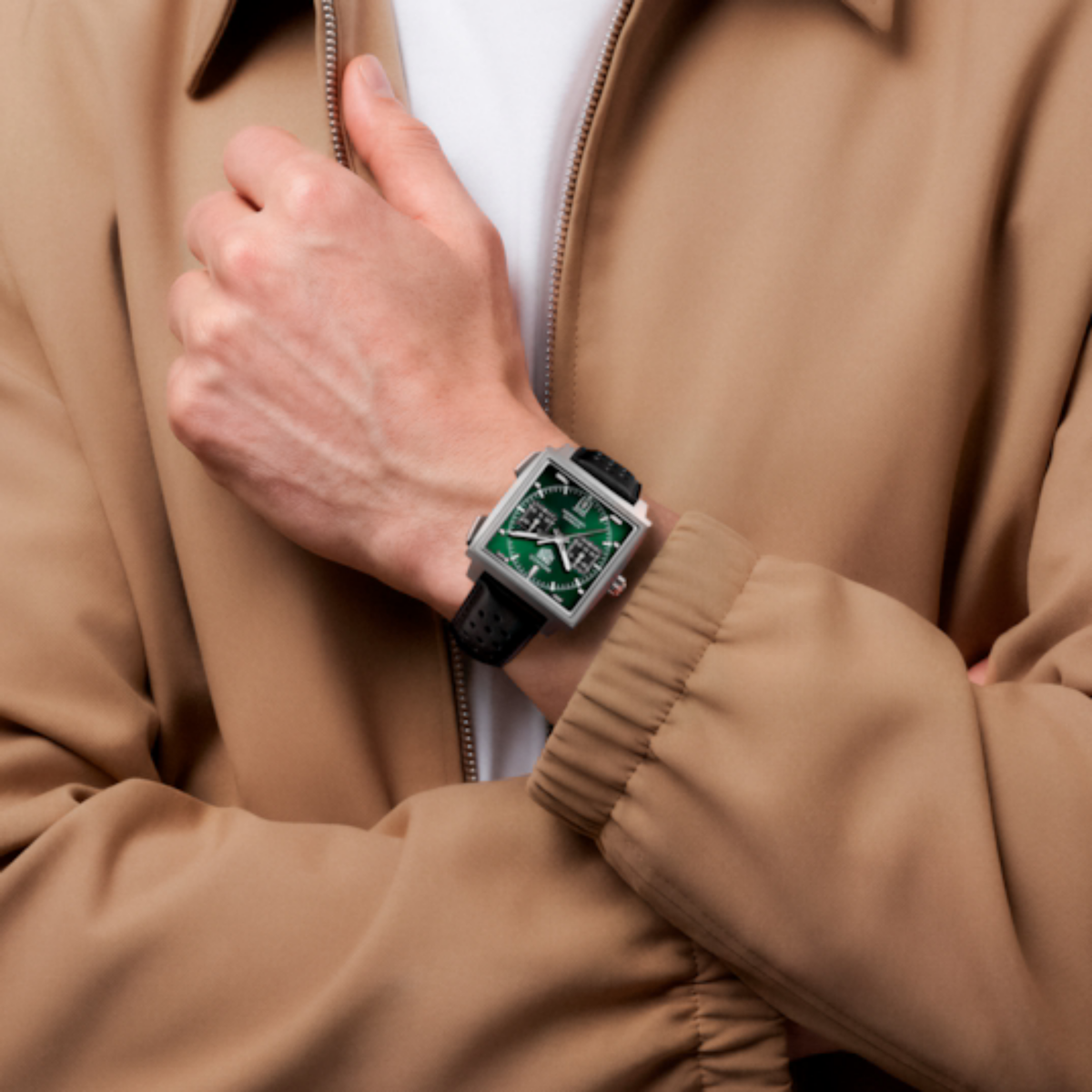 TAG Heuer Monaco Chronograph with green dial and black leather strap worn on the wrist, paired with a tan jacket.