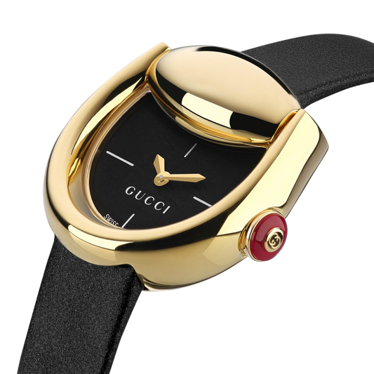 Close-up of the Gucci Horsebit watch featuring a black dial, yellow gold-plated case and signature red resin crown.