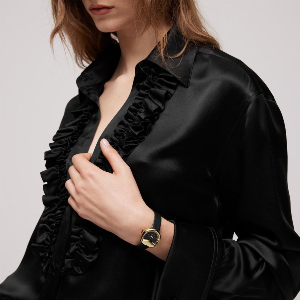 Gucci Horsebit ladies' watch worn on the wrist with a yellow gold-plated case, black dial and black leather strap.