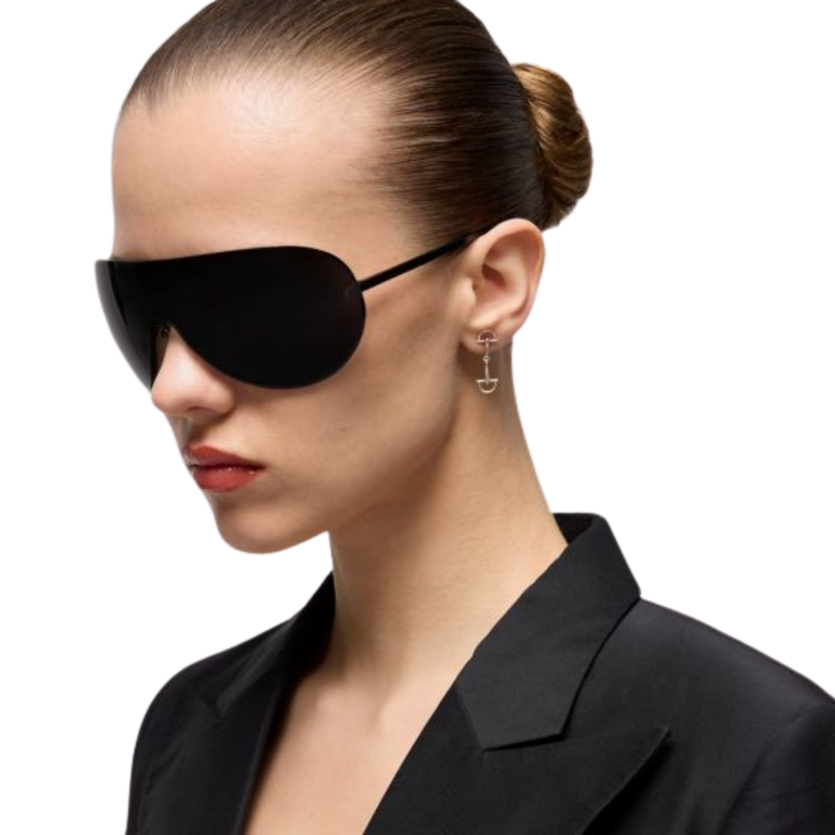 Model wearing Gucci Staffa sterling silver drop earrings featuring the brand's flexible stirrup motif, paired with a black blazer and oversized shield sunglasses for a modern, minimalist look.