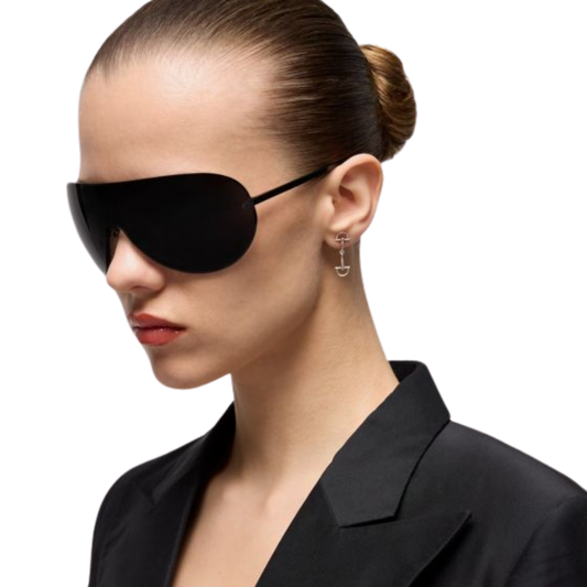 Model wearing Gucci Staffa sterling silver drop earrings featuring the brand's flexible stirrup motif, paired with a black blazer and oversized shield sunglasses for a modern, minimalist look.
